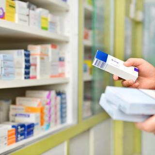 Pharmacist holding prescription boxes beside shelves